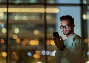 Young man text messaging on cell phone indoors at night.
