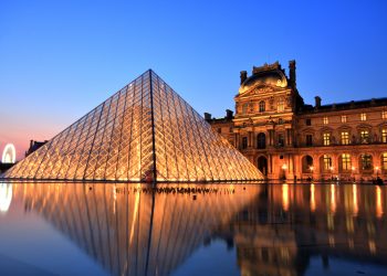 Paris, France - July 6, 2013: Illuminated Louvre museum during sunset in Paris. The Pyramid is the main entrance to the Louvre Museum.