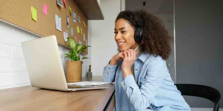 Smiling young african american teen girl wear headphones video calling on laptop. Happy mixed race pretty woman student looking at computer screen watching webinar or doing video chat by webcam.