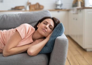 Young mom lying on on pillow on couch, resting, sleeping after completing house working. Woman napping on sofa in living room, feel fatigue, relaxing. Leisure, lazy time concept.