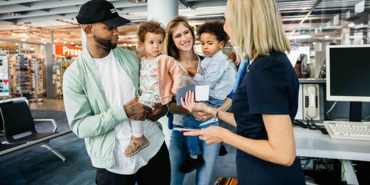 A family with two young children getting ready to board a flight together, letting an airport staff member check their passports and boarding passes at the gate.