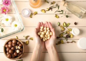 Female hands with macadamia nuts and natural cosmetics on wooden background
