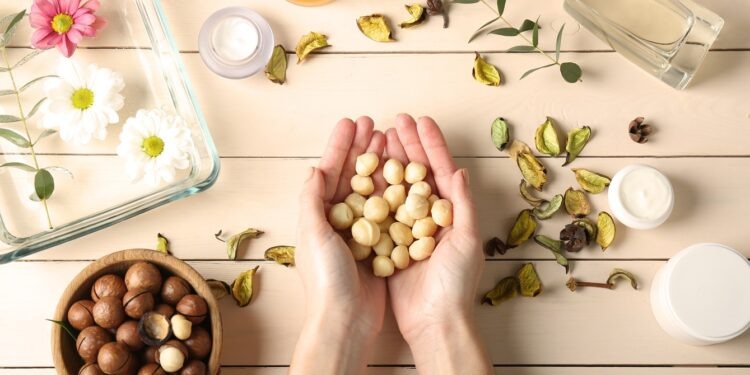 Female hands with macadamia nuts and natural cosmetics on wooden background