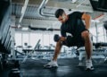 Man sitting on one gym machine and doing biceps.