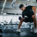 Man sitting on one gym machine and doing biceps.
