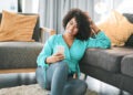 Cropped shot of an attractive young woman sitting on her living room floor and using her cellphone at home