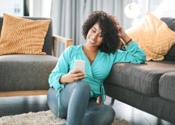 Cropped shot of an attractive young woman sitting on her living room floor and using her cellphone at home