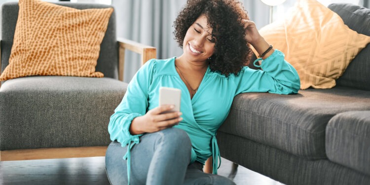 Cropped shot of an attractive young woman sitting on her living room floor and using her cellphone at home