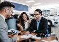 Middle age couple choosing and buying car at car showroom. Car salesman helps them to make right decision. Man signs buyers contract.