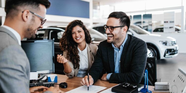 Middle age couple choosing and buying car at car showroom. Car salesman helps them to make right decision. Man signs buyers contract.