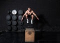 Young strong fit sweaty muscular man with big muscles doing box jump workout in the gym as hardcore cross training
