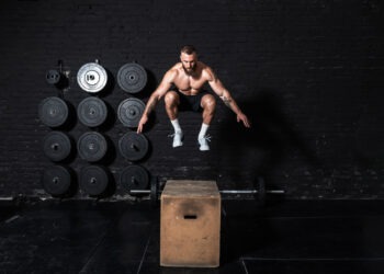 Young strong fit sweaty muscular man with big muscles doing box jump workout in the gym as hardcore cross training
