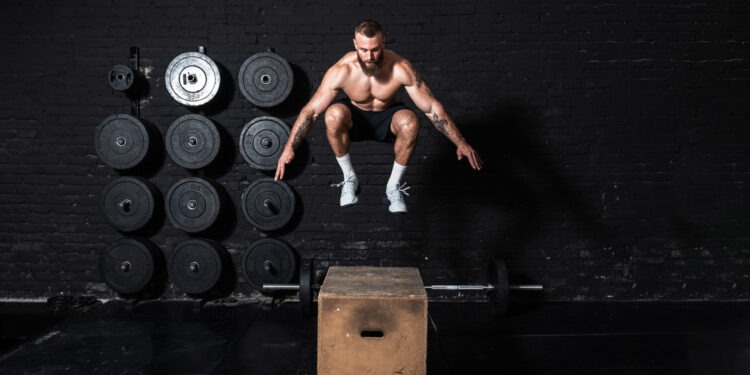 Young strong fit sweaty muscular man with big muscles doing box jump workout in the gym as hardcore cross training