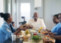 A multi-generational African ethnicity family eating together and a female passing the plate of barbequed meat to the senior malke at the head of the table Strand Cape Town South Africa