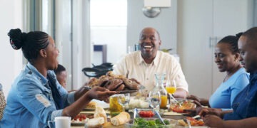 A multi-generational African ethnicity family eating together and a female passing the plate of barbequed meat to the senior malke at the head of the table Strand Cape Town South Africa