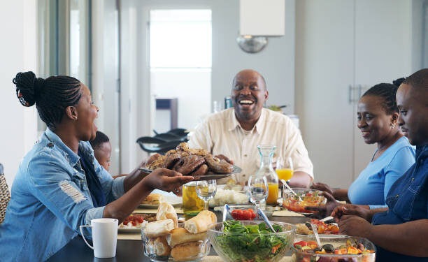 A multi-generational African ethnicity family eating together and a female passing the plate of barbequed meat to the senior malke at the head of the table Strand Cape Town South Africa