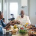 A multi-generational African ethnicity family eating together and a female passing the plate of barbequed meat to the senior malke at the head of the table Strand Cape Town South Africa