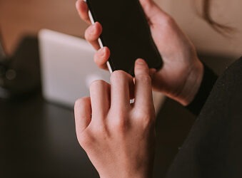 Woman;s hand holding cellphone ready to unlocked it. Girl using telephone near table wit computer in office