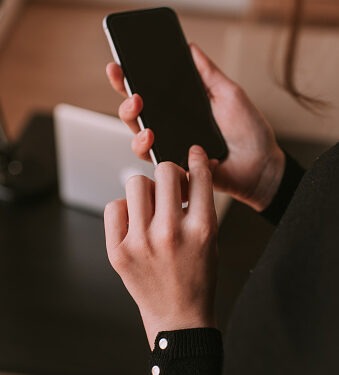 Woman;s hand holding cellphone ready to unlocked it. Girl using telephone near table wit computer in office